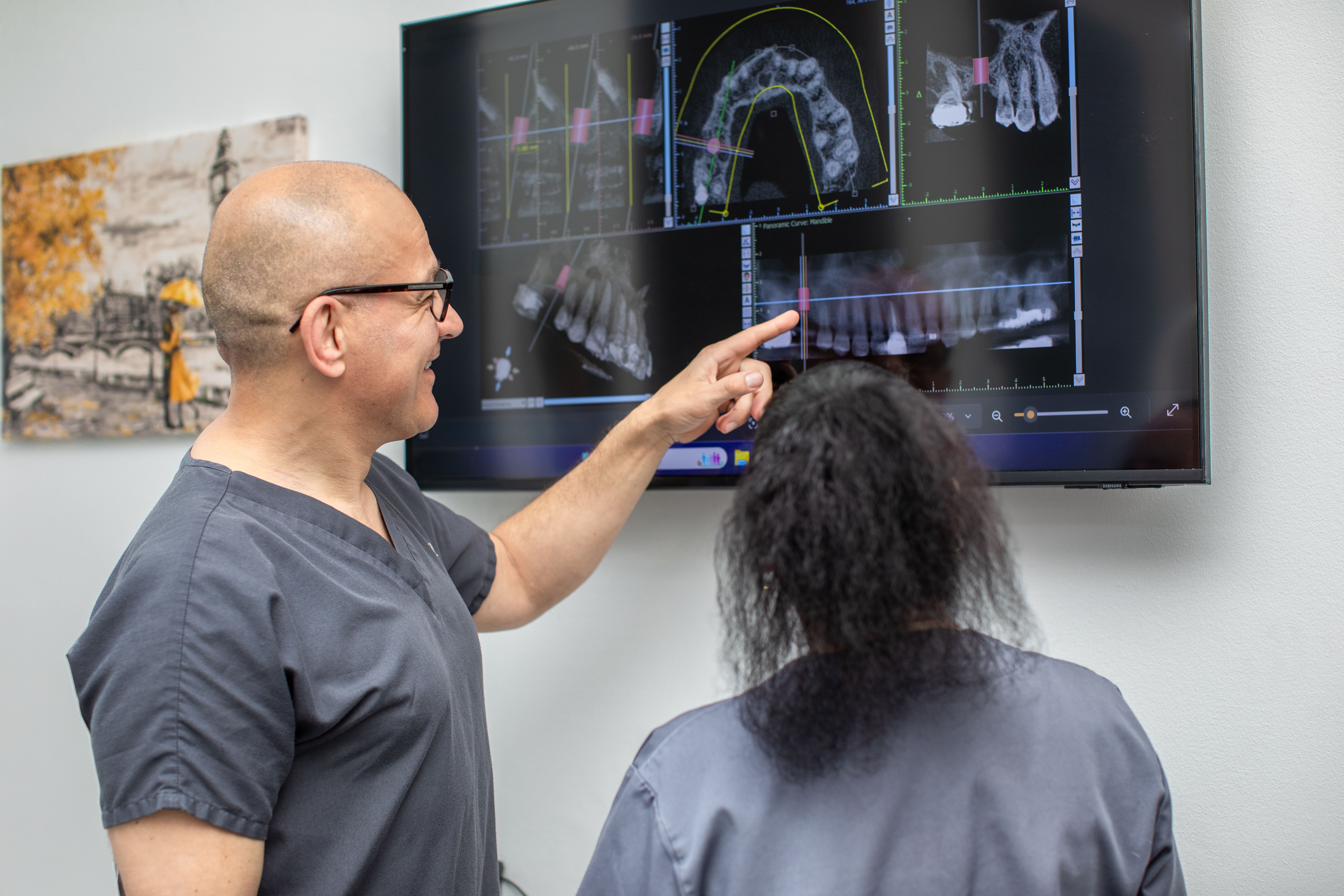 A dentist points to dental X-rays on a screen, explaining them to a patient.