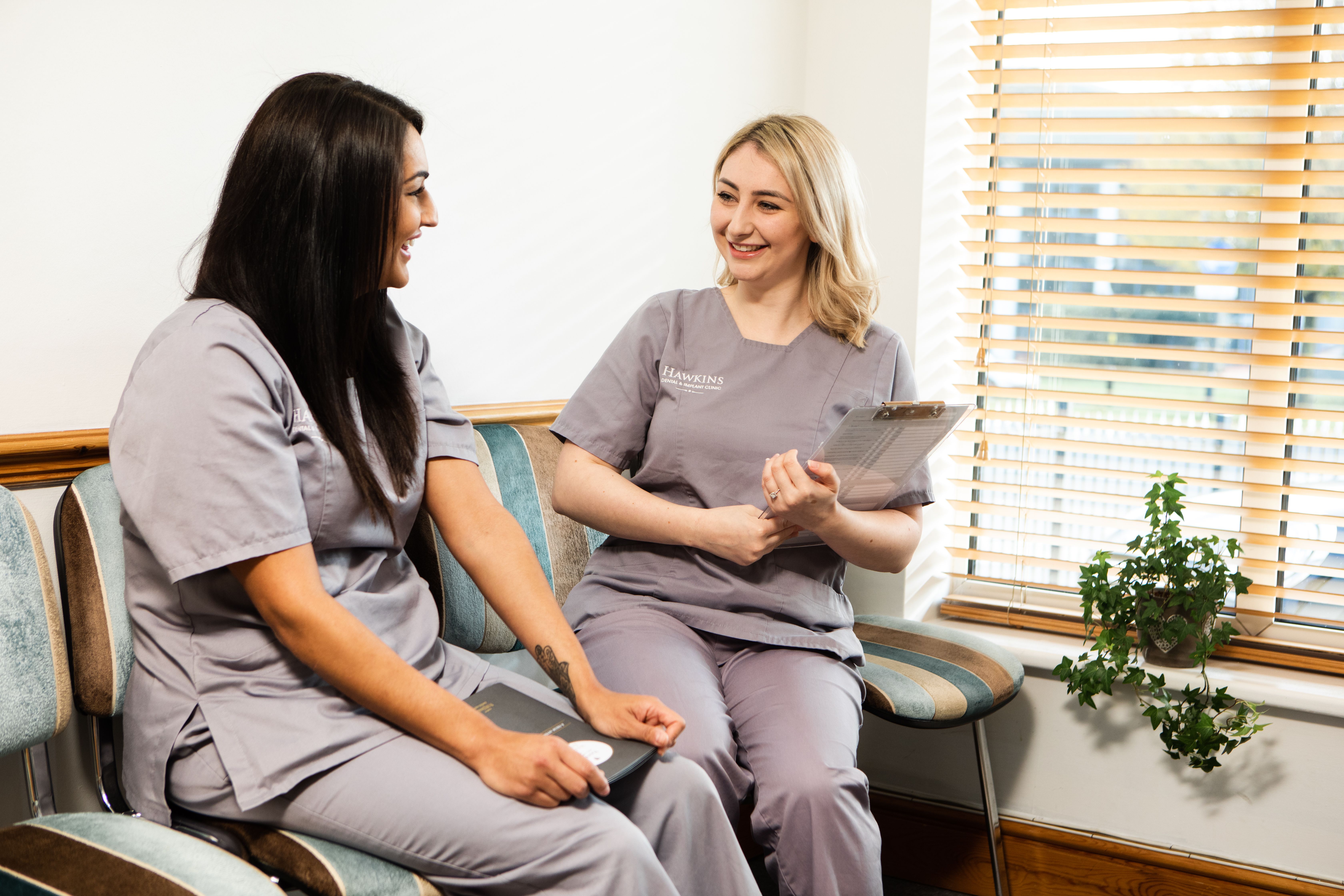 two nurses are sitting in a waiting room talking to each other .