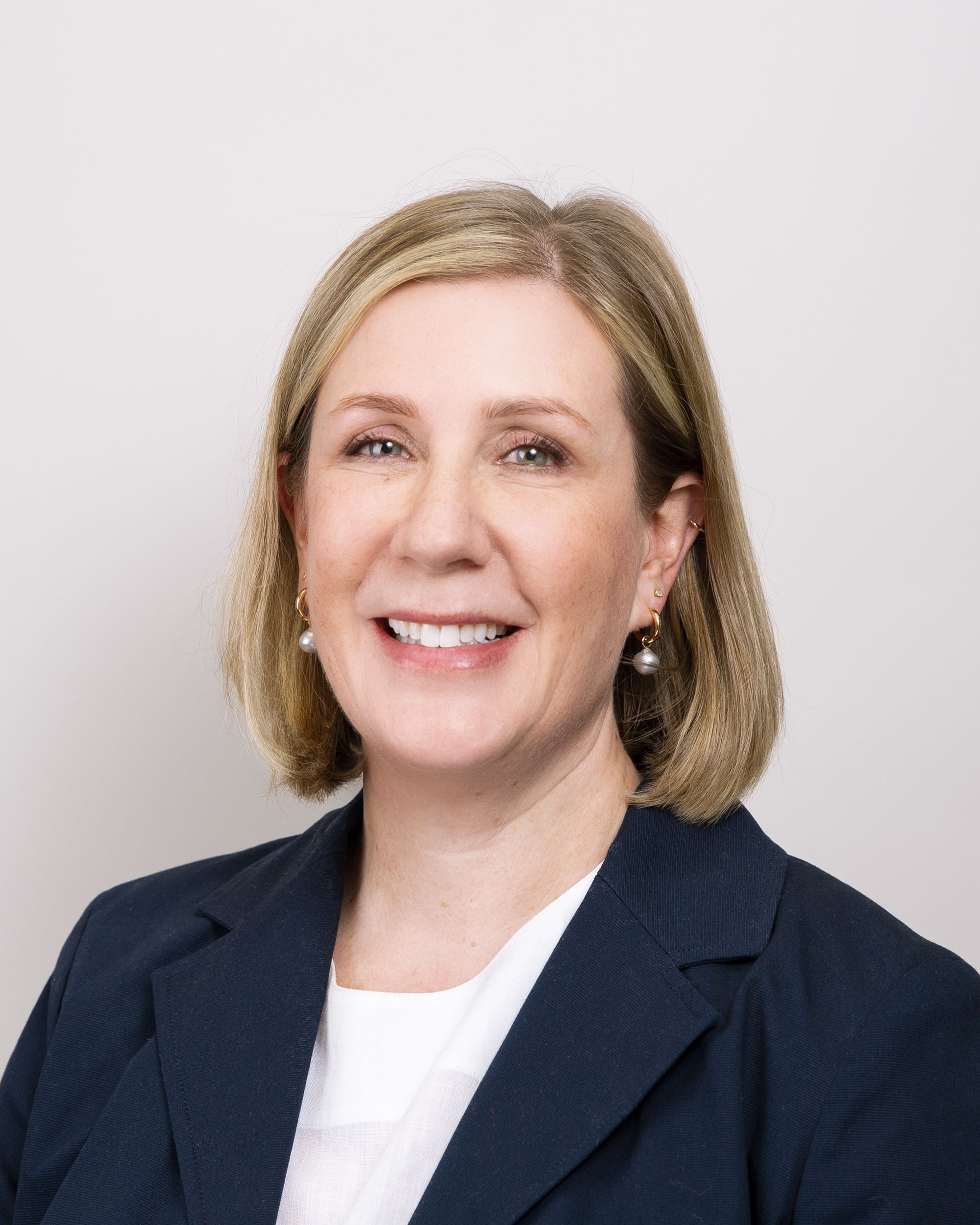 a woman wearing a blue jacket and pearl earrings smiles for the camera .