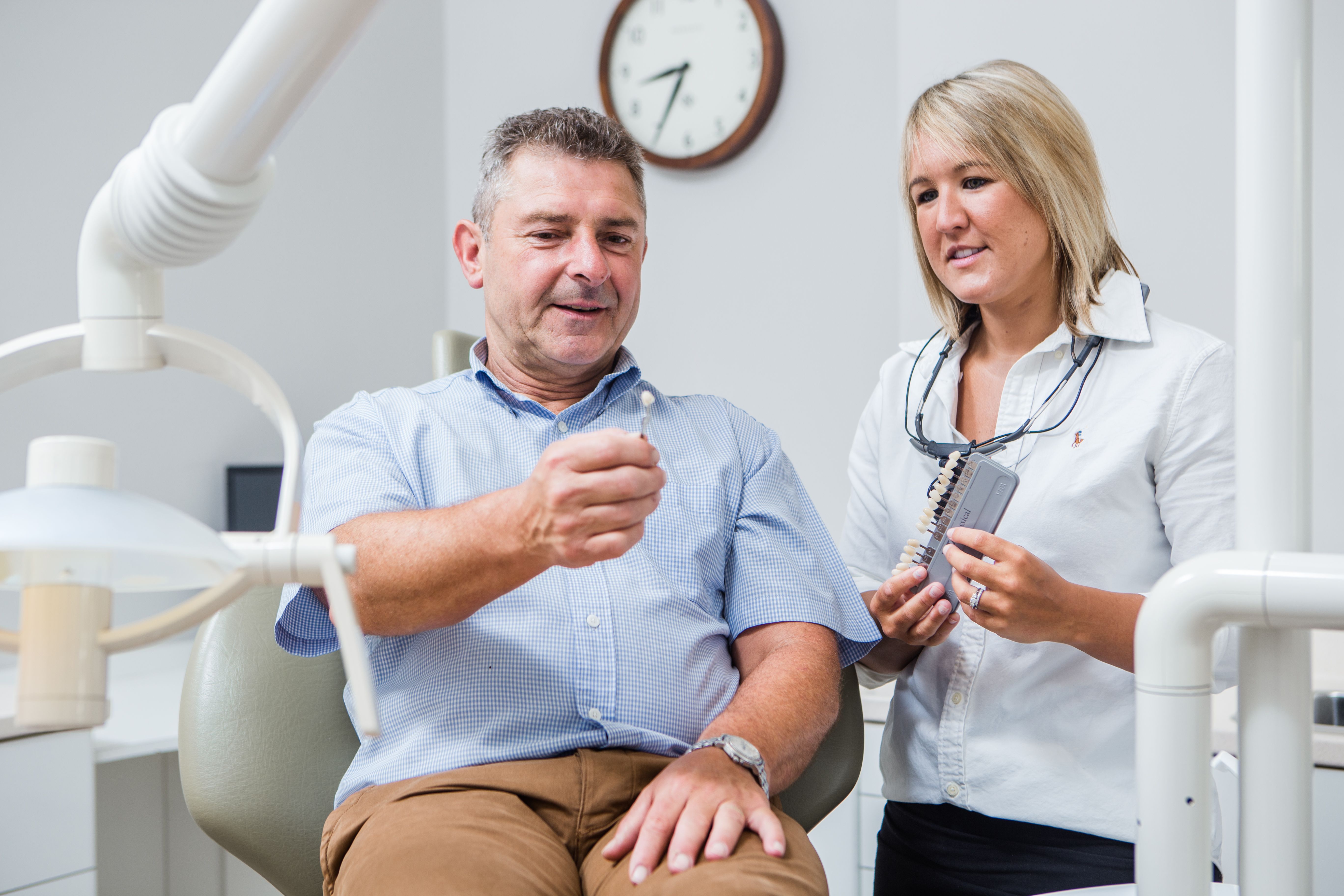 a man is sitting in a dental chair while a woman stands next to him .