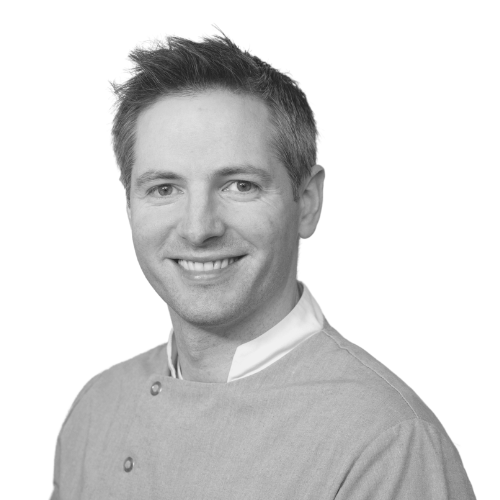 Black and white headshot of a smiling man in medical scrubs.