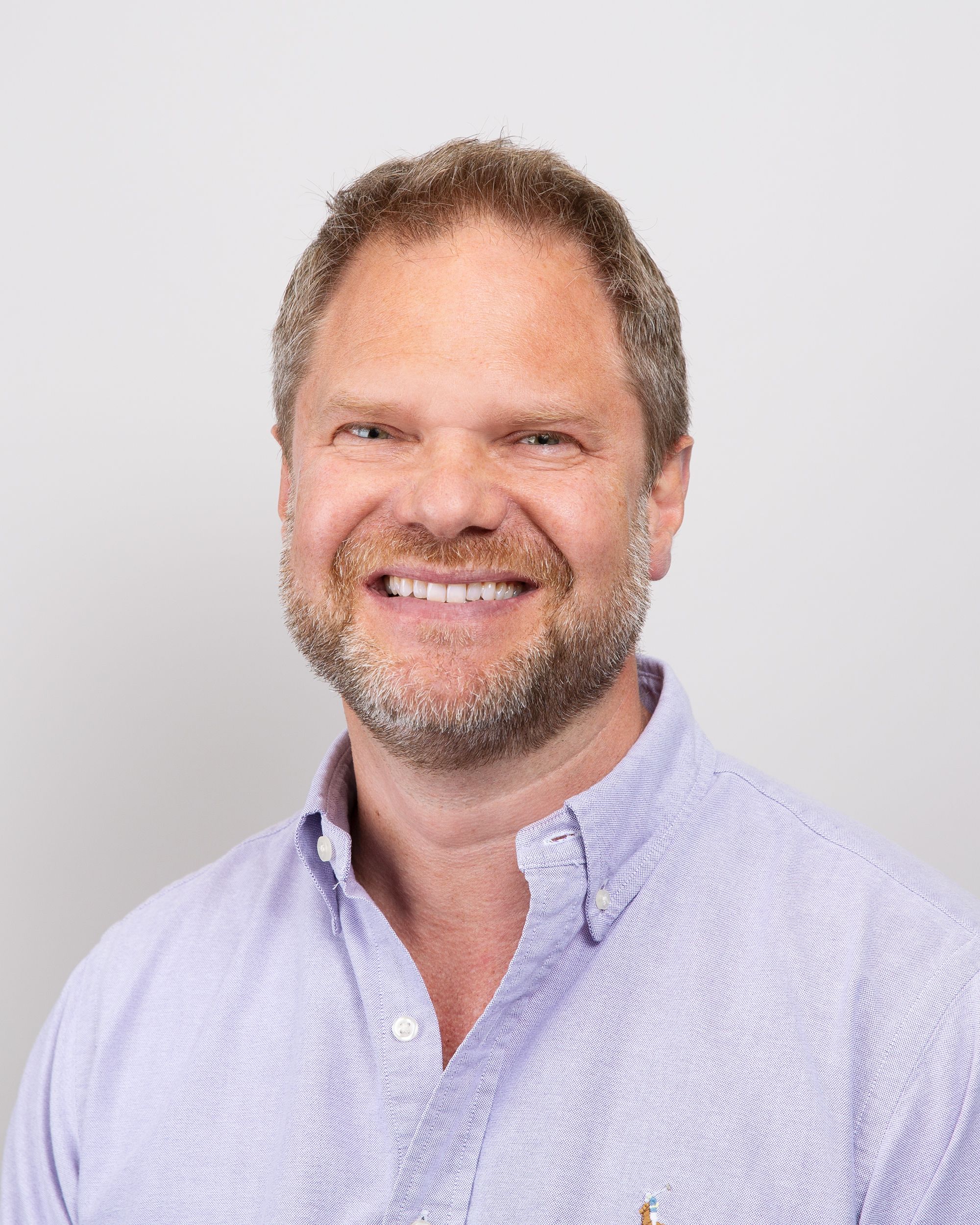 a man with a beard is smiling for the camera while wearing a purple shirt .