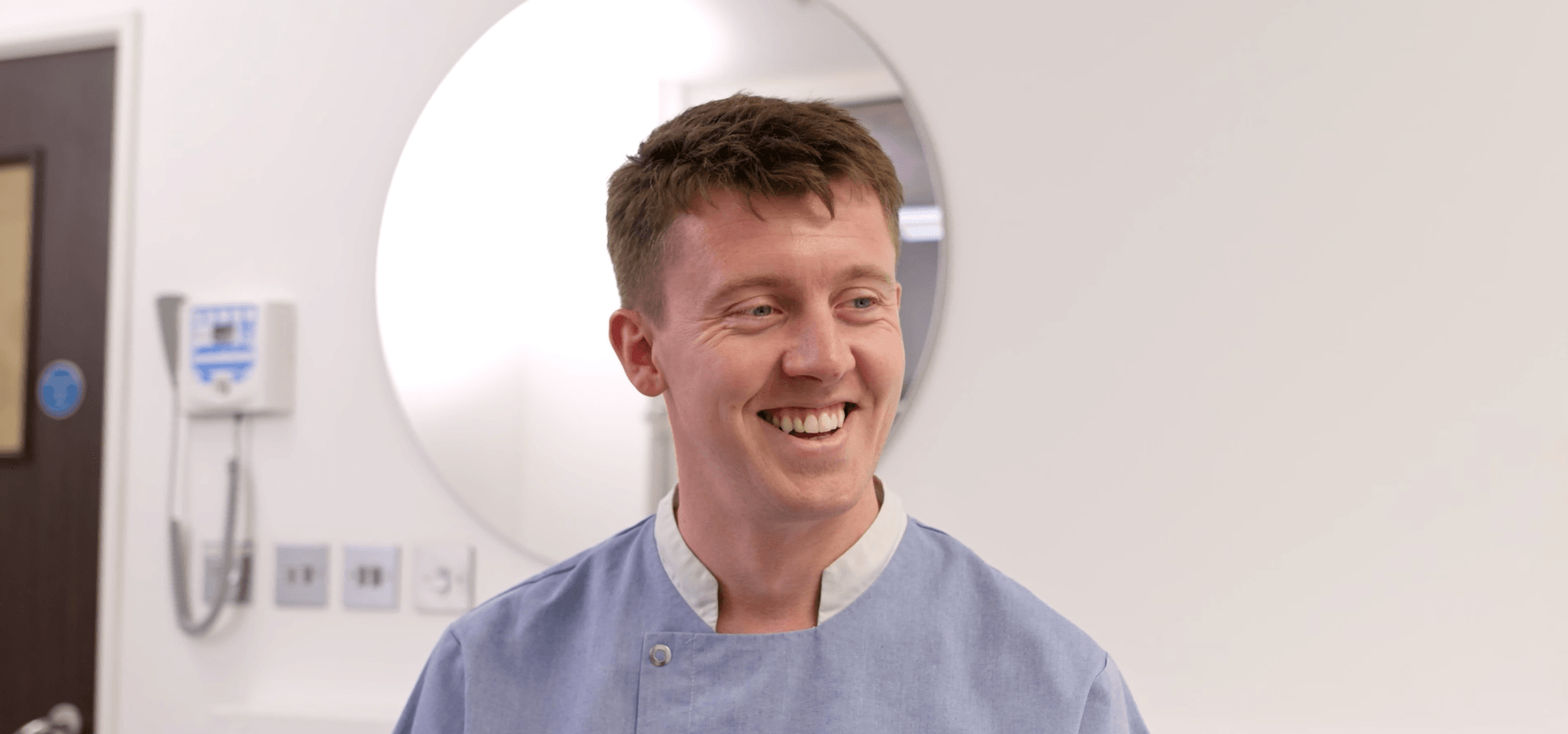Smiling man in a light blue uniform.
