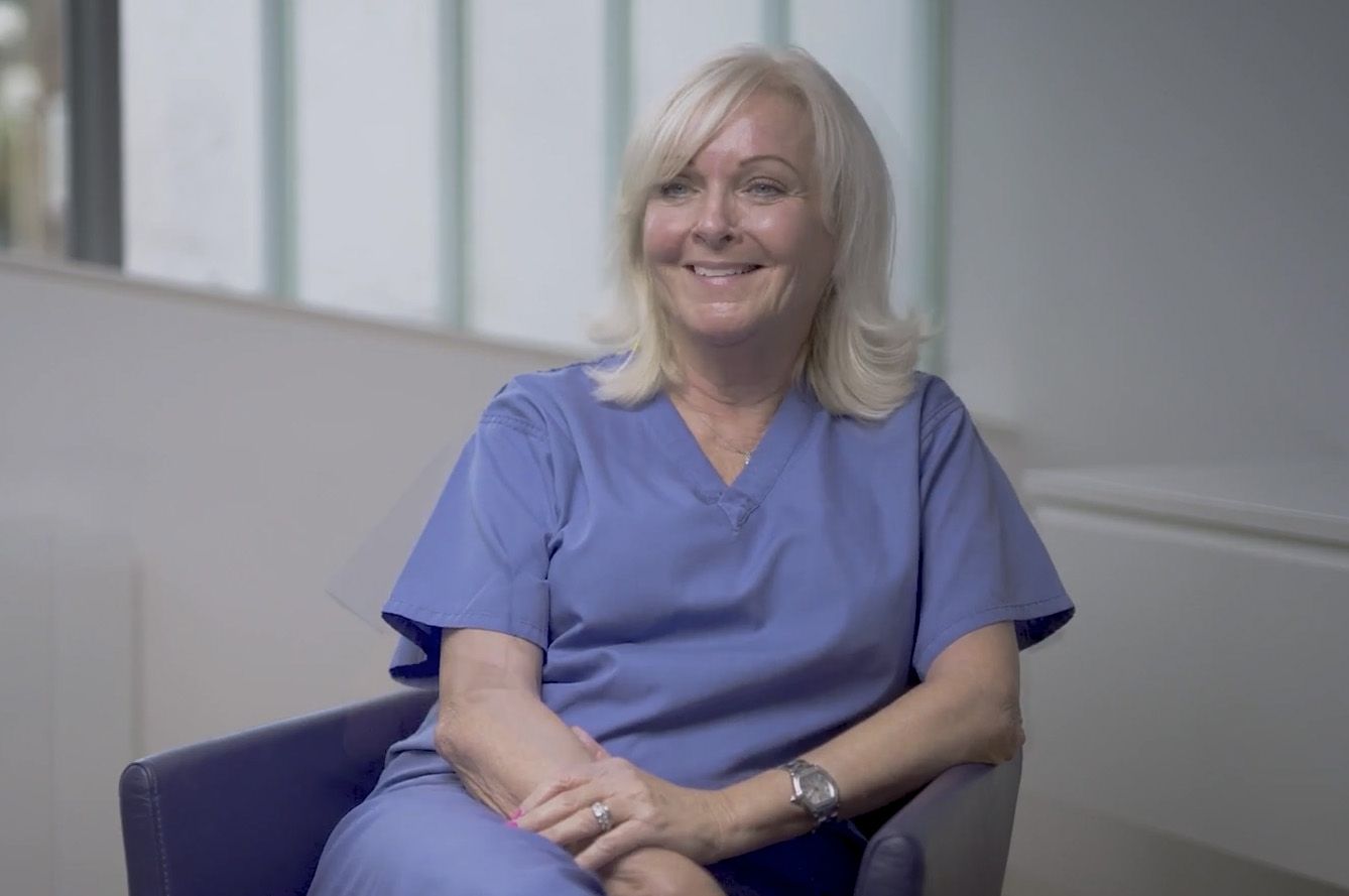 a woman in a blue scrub is sitting in a chair and smiling .