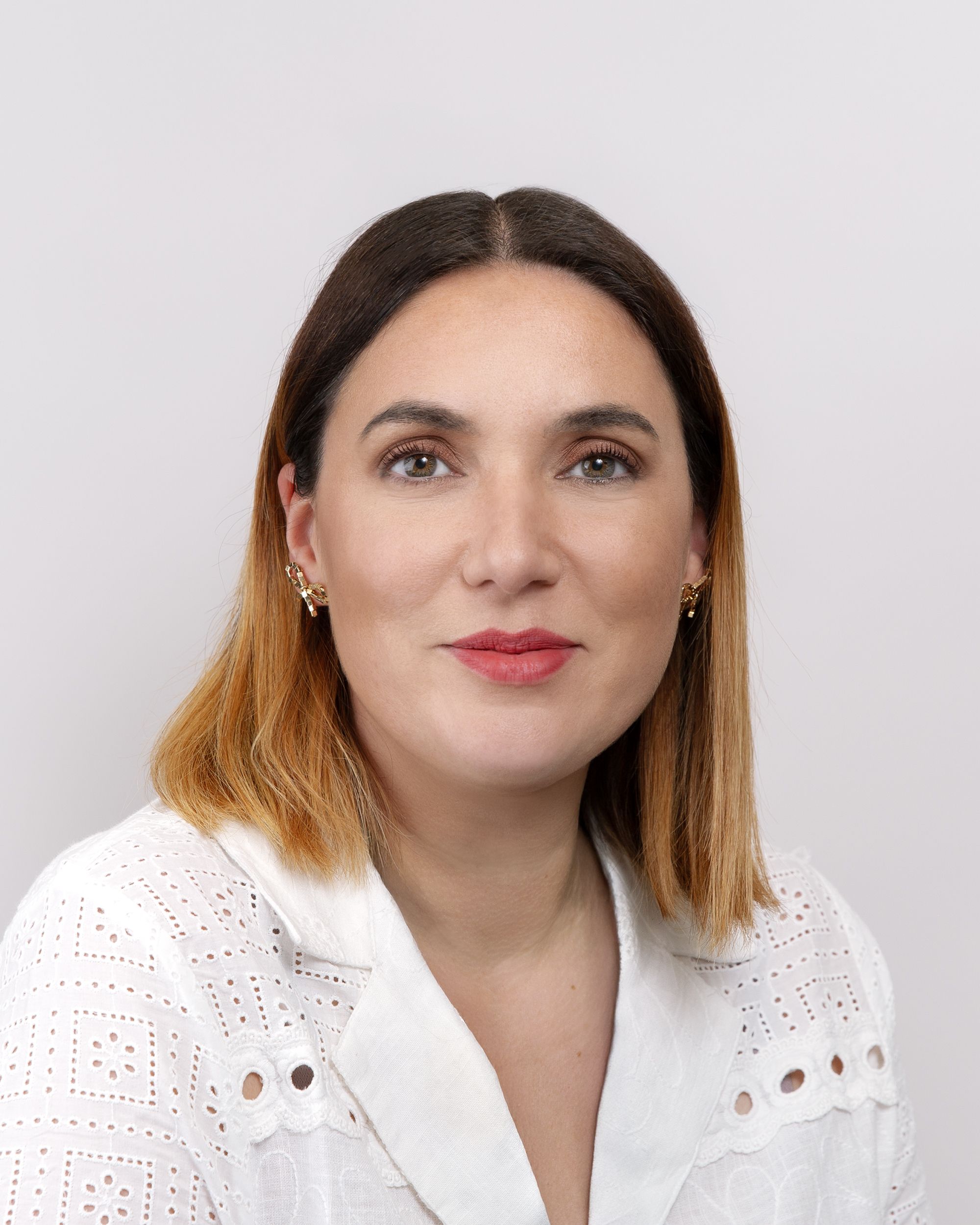 a woman wearing a white shirt and earrings is smiling for the camera .