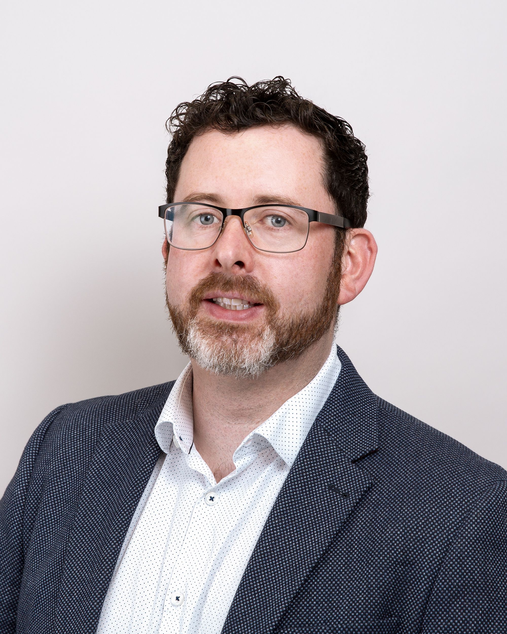 a man with glasses and a beard is wearing a suit and a white shirt .